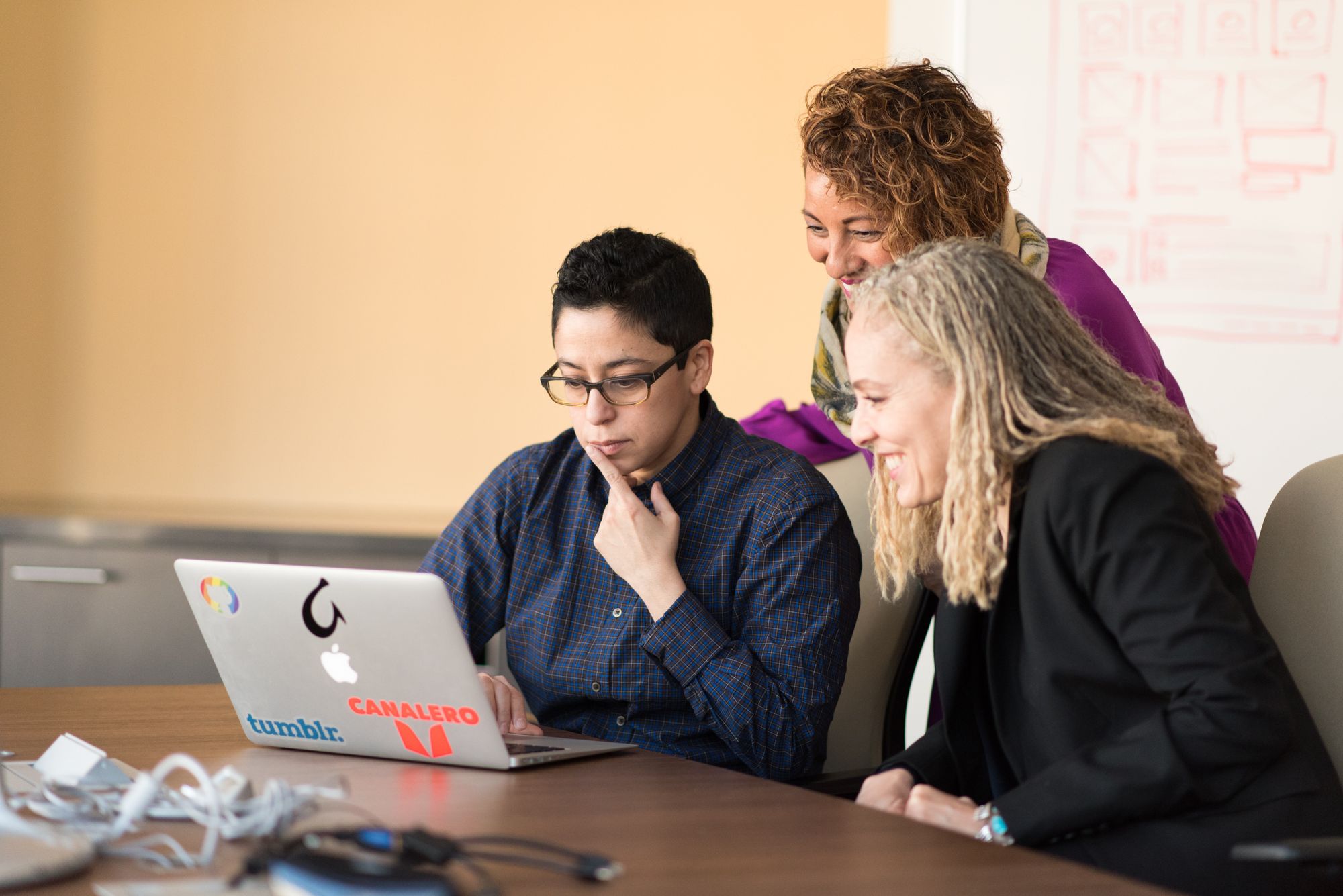 three people look at a laptop to collaborate